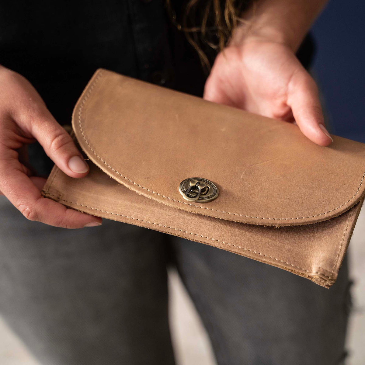 Betty Jean Women’s Fine Leather Envelope Clutch in tan, held by a person, showcasing its sleek design and clasp.