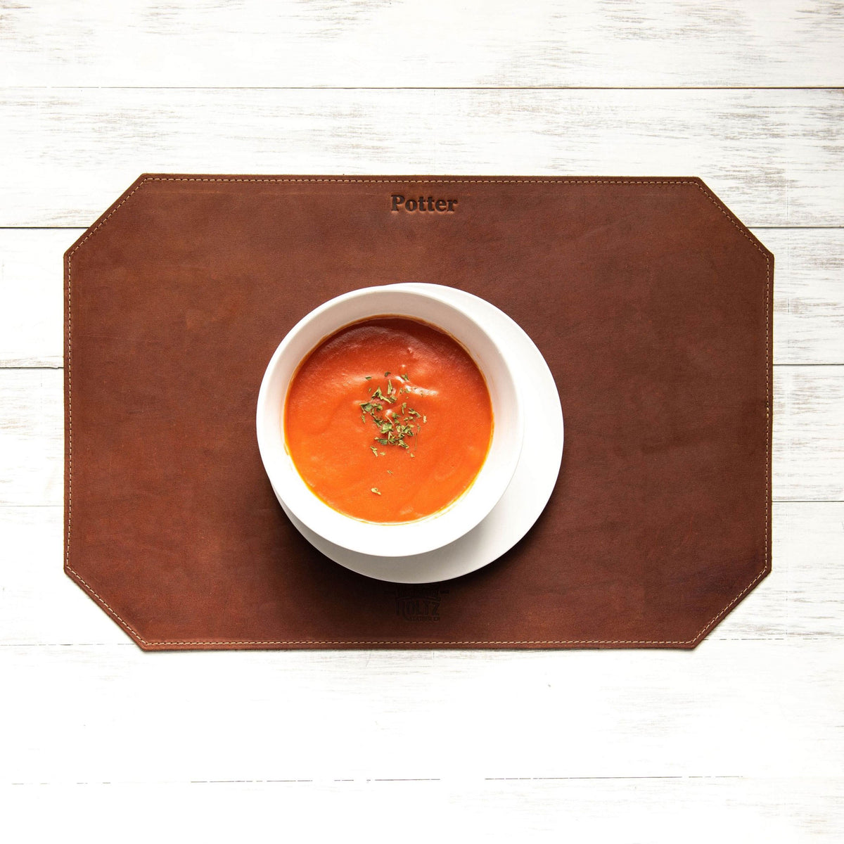 Beveled edge personalized fine leather placemat in brown with a bowl of soup on top.