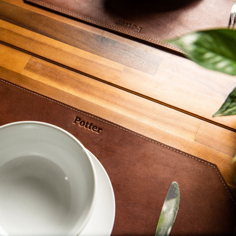 Beveled edge personalized fine leather placemat in brown with custom engraving on a wooden table setting.