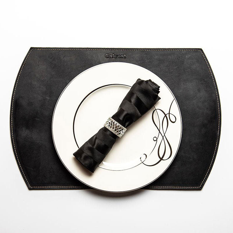 Straight edged oval personalized fine leather placemat in black with a white plate and black napkin.