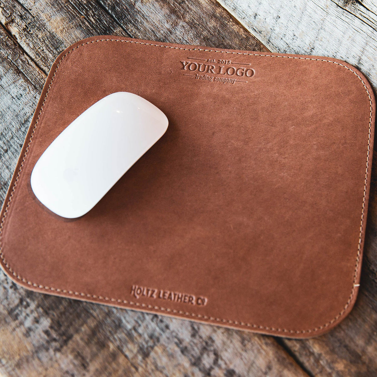 Leather mousepad with custom logo, featuring a sleek design and a white mouse on a rustic wooden surface.