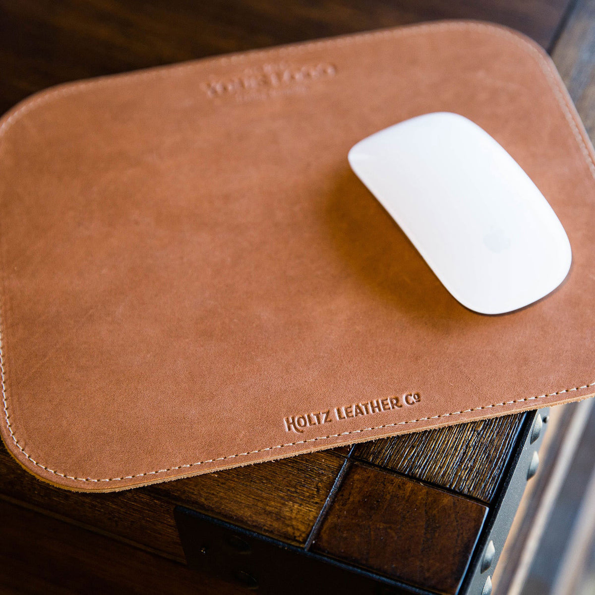 Leather mousepad with custom logo, featuring a sleek design and a white mouse on a wooden surface.
