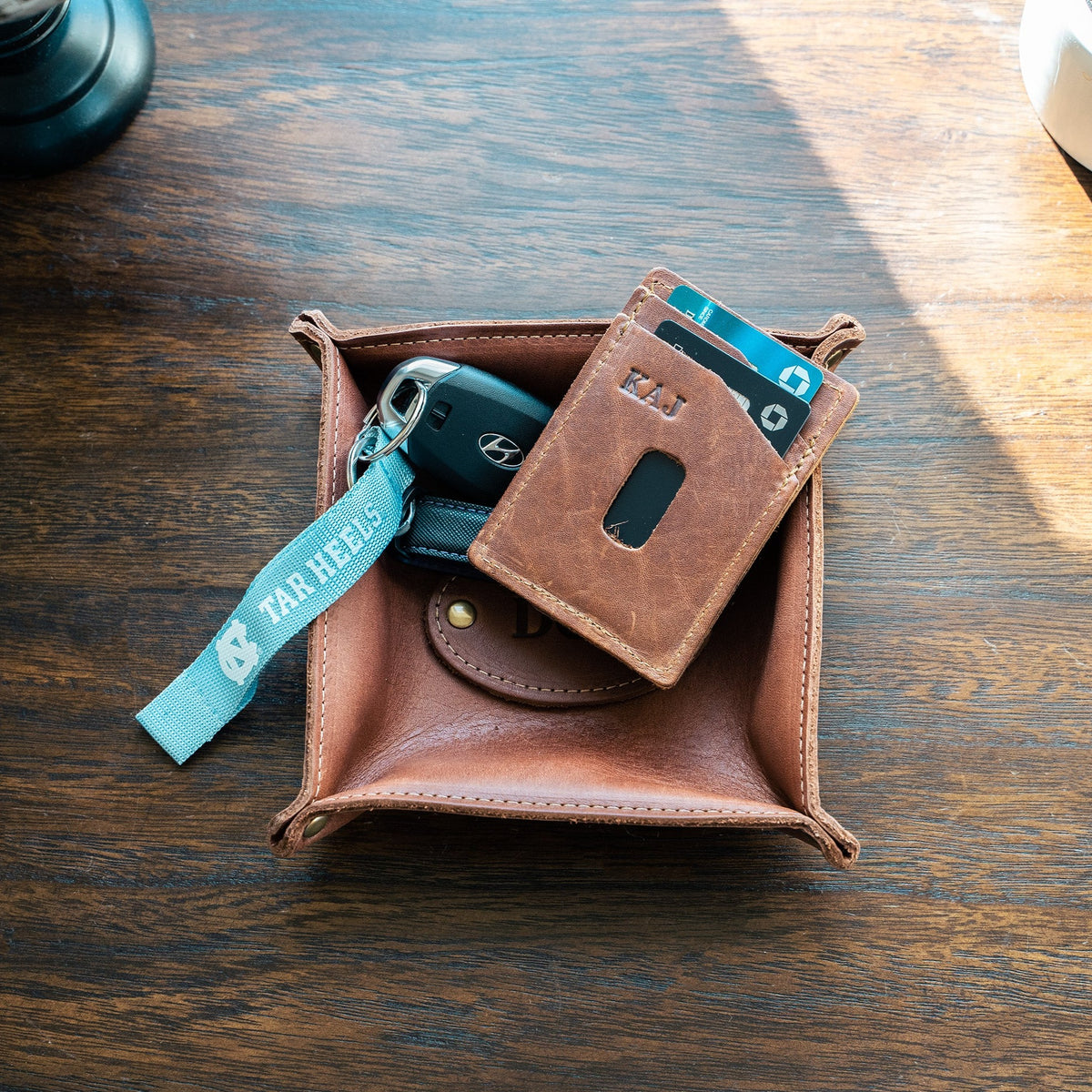 Monticello Fine Leather Personalized Desk Valet Caddy Tray in brown, holding keys and a cardholder on a wooden surface.