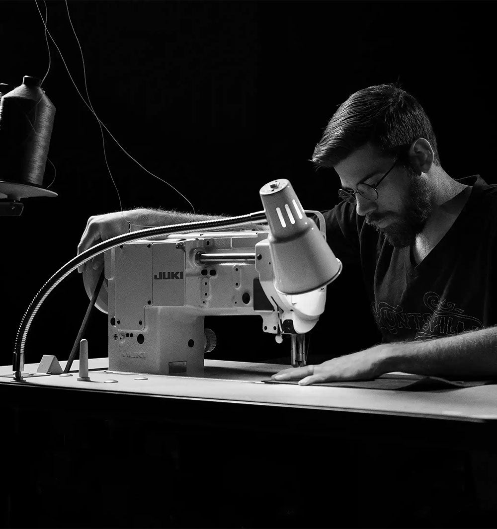 Man operating a sewing machine at a table with large spools of thread.