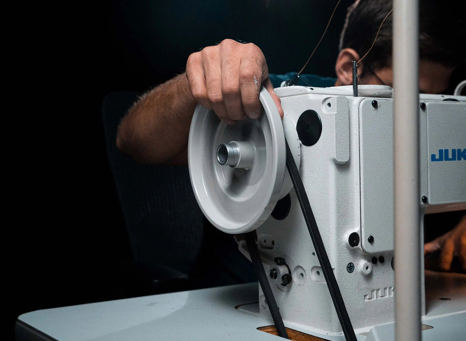 Close-up of a worker adjusting the handwheel on a white industrial sewing machine.
