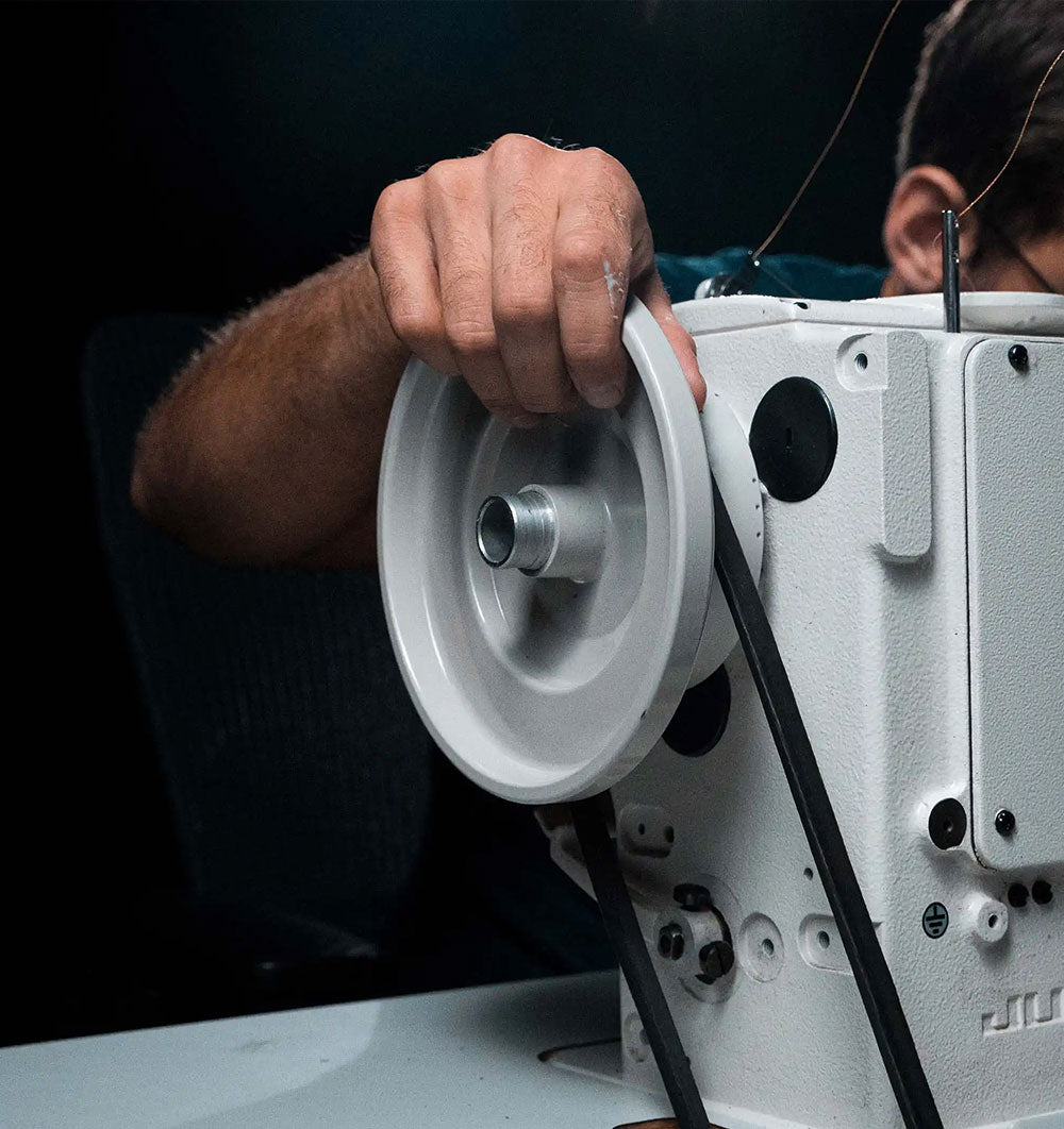 Close-up of a worker adjusting the handwheel on a white industrial sewing machine.