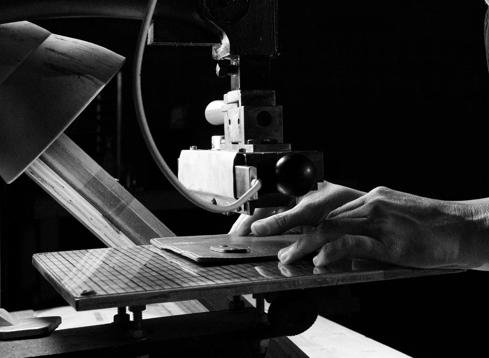 Black-and-white close-up of a hand guiding material beneath a vintage machine.