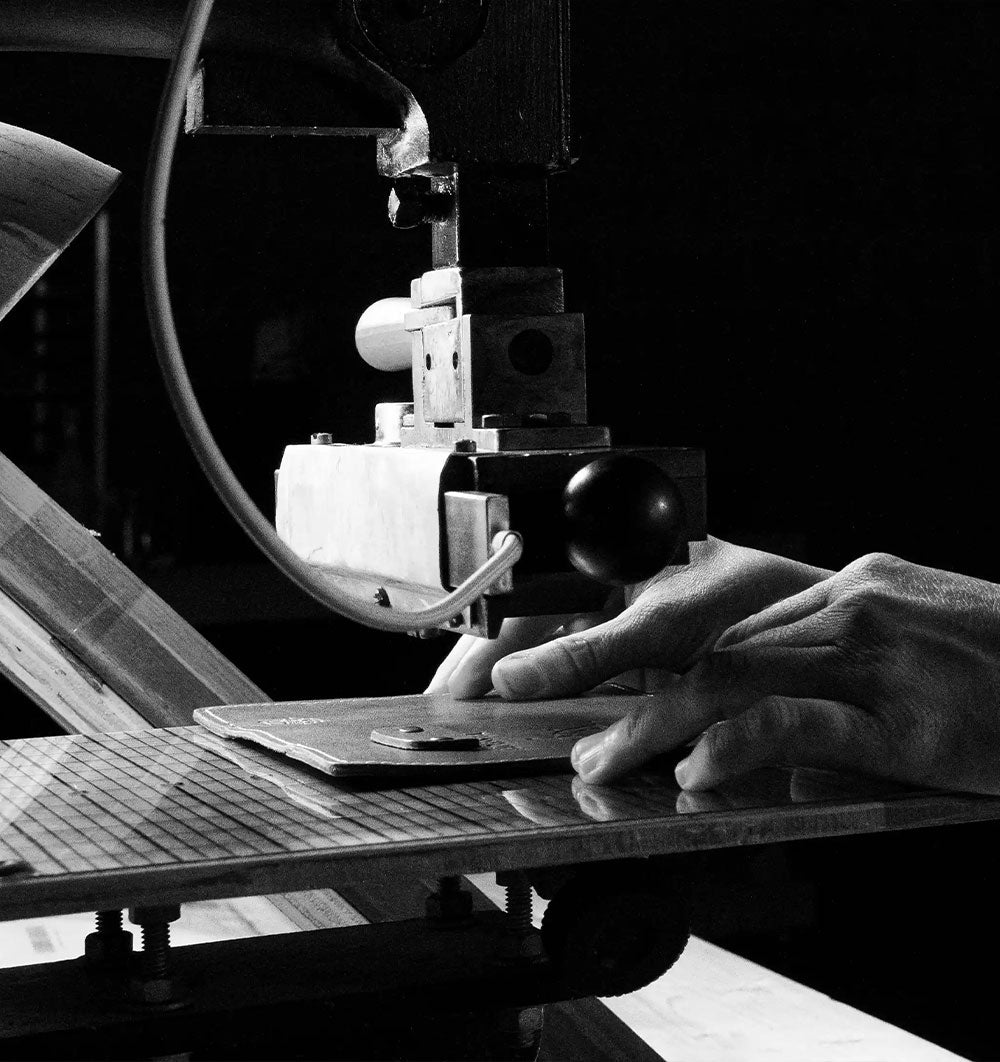 Black-and-white close-up of a hand guiding material beneath a vintage machine.